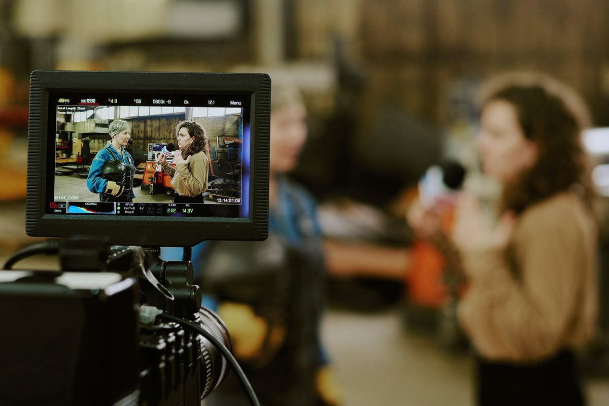 Creator and colleague being filmed by a professional camera with a monitor displaying the scene inside a studio